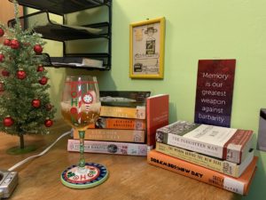 Image of books piled on a desk with a glass of wine.