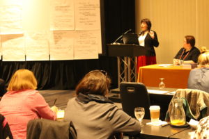 Susan leading a workshop, in front of a list of ideas generated by the audience.