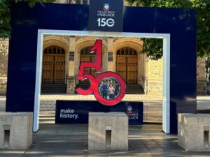 An entryway to the University of Adelaide campus, celebrating the university's 150th anniversary. A three-dimensional "150" sits atop a blue platform with the words "Make History."