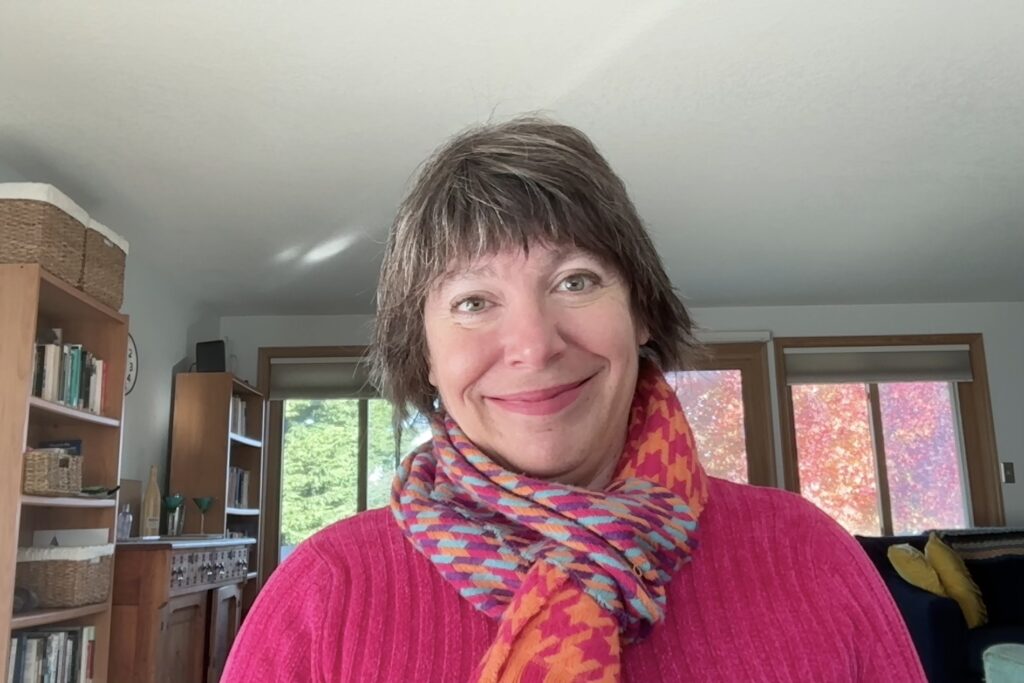 Susan Ferentinos, smiling in front of a window showing autumn leaves